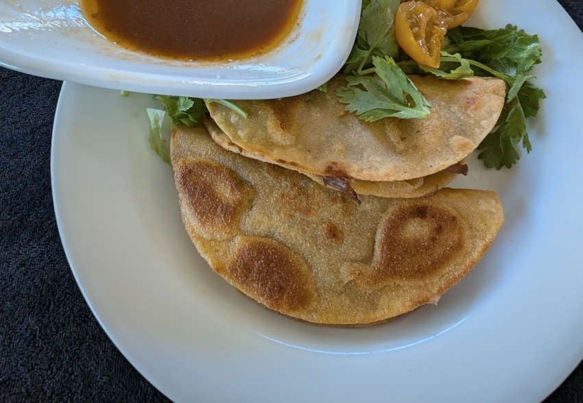 photo of two birria tacos on a white plate with broth